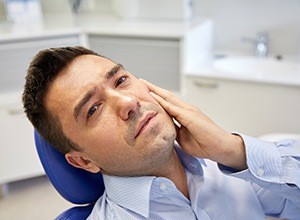 Man in dental chair holding cheek in pain